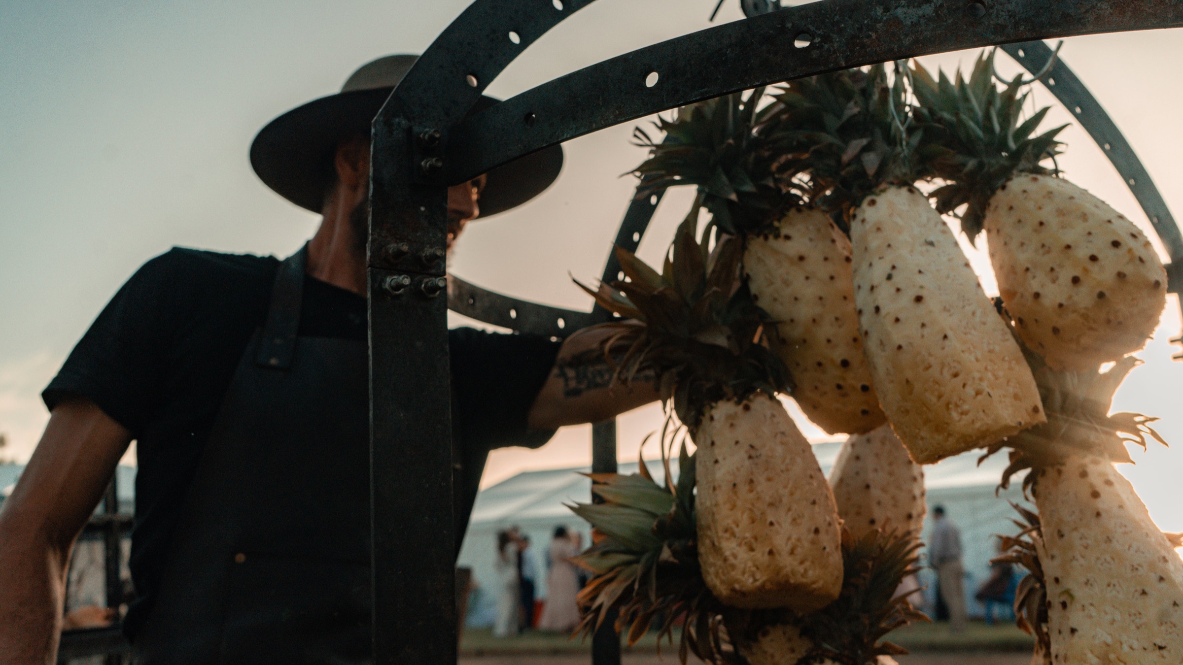 An asador tending pineapples hung over the fire at dusk
