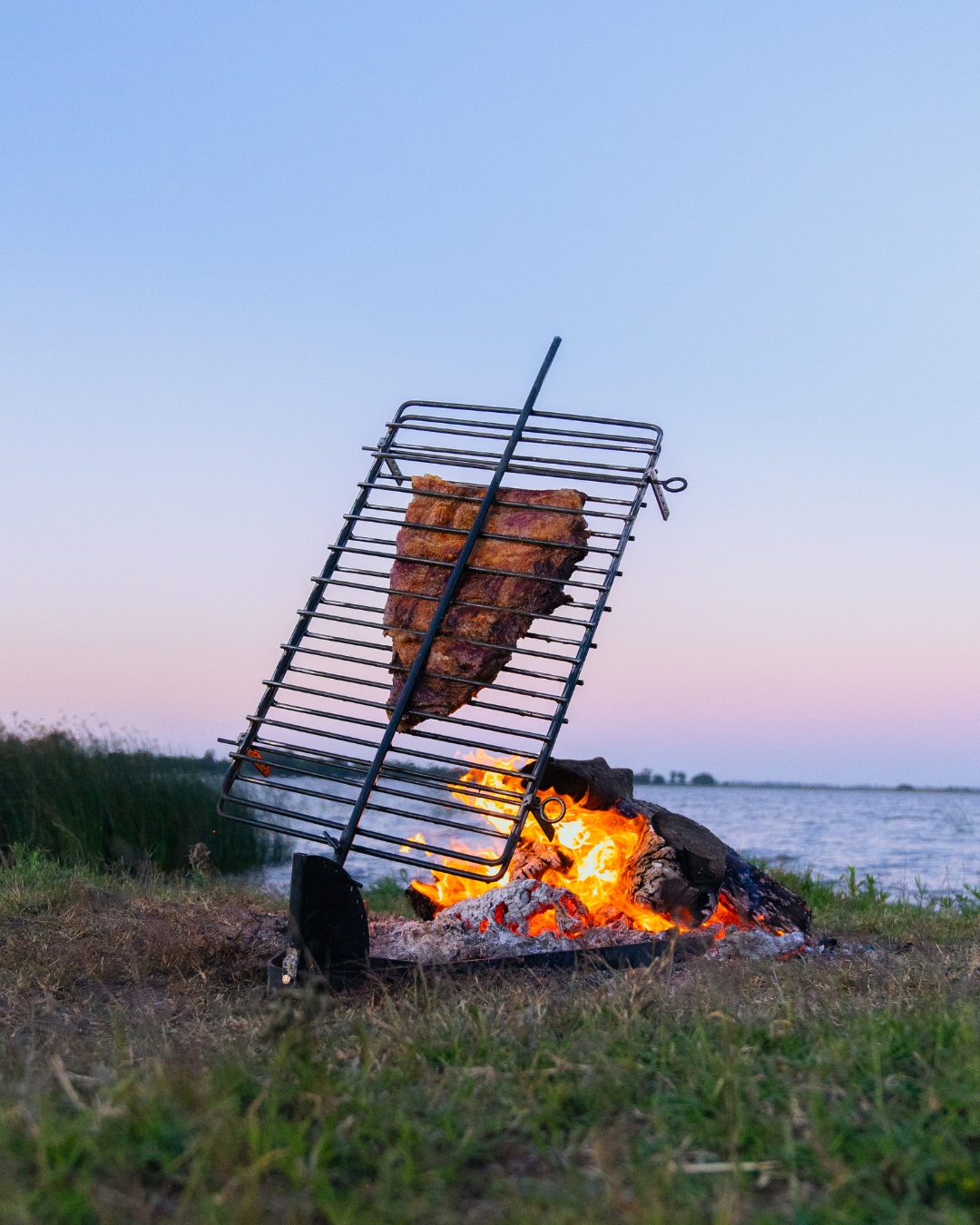 A Gran Campero grill cooking ribs beside the water at dusk